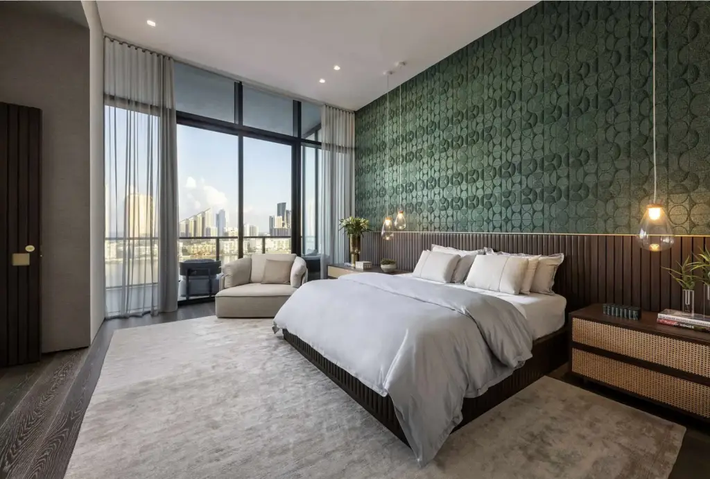 Modern luxury bedroom featuring a green textured accent wall, floor-to-ceiling windows with city skyline views, neutral furnishings, and pendant lighting.