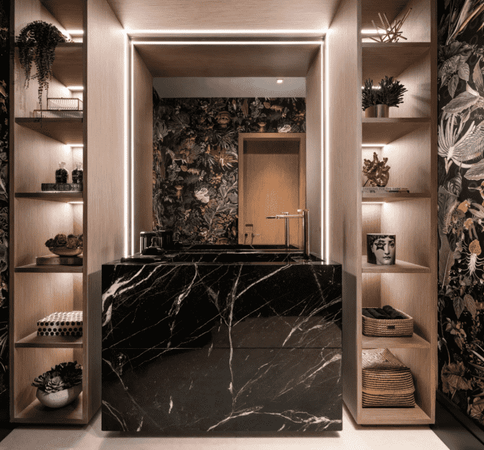 Luxe powder room featuring dramatic botanical wallpaper, illuminated wood shelving with curated decor, and a striking black marble vanity with modern fixtures.