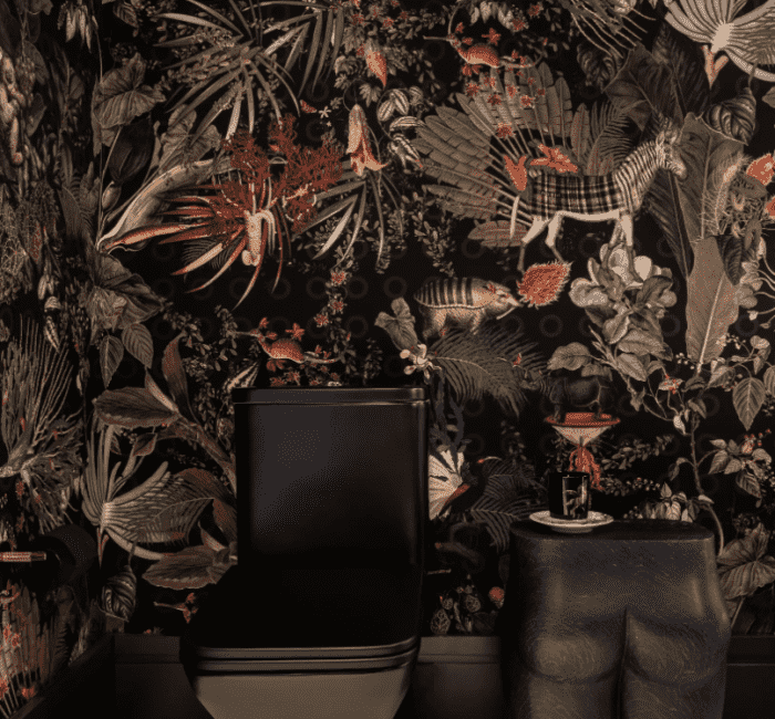 Bold powder room featuring a matte black toilet, sculptural side table, and dramatic jungle-themed wallpaper with exotic flora and fauna.