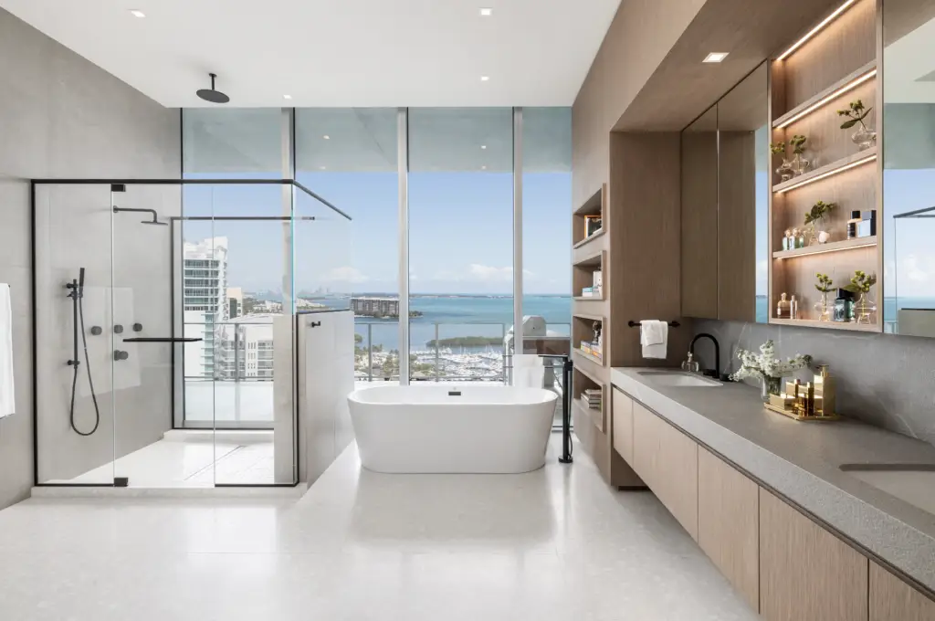 Modern high-rise bathroom with floor-to-ceiling windows, freestanding tub, glass-enclosed shower, and built-in wood cabinetry.